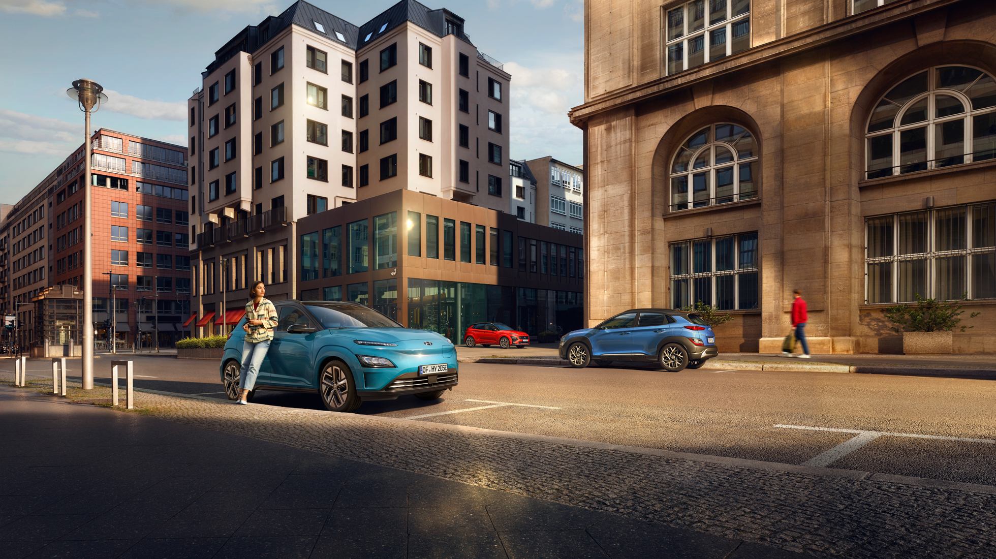 Nové kompaktní SUV Hyundai KONA Electric zaparkované na druhé straně ulice proti SUV Hyundai KONA.